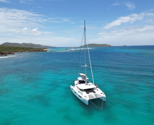 Catamaran anchored in turquoise Caribbean waters with scenic island background, perfect for sailing and boating adventures.